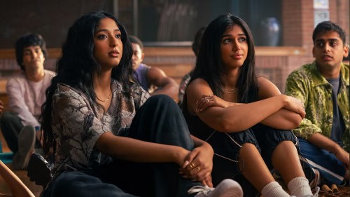 Two pretty, young South Asian women with long dark hair sit next to each other on the floor, listening to someone speak 